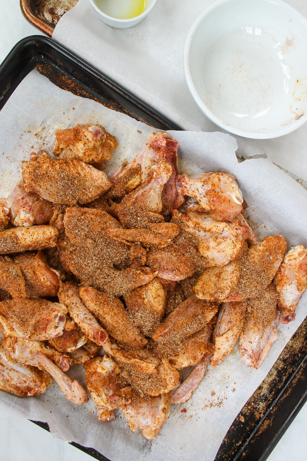 Raw chicken wings on a sheet pan covered in dry rub seasoning.
