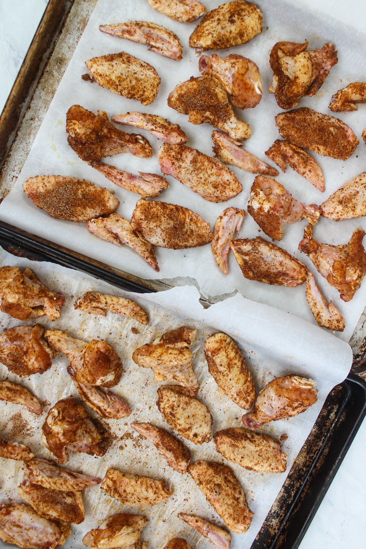 Two pan of chicken wings seasoned with dry rub ready to bake.