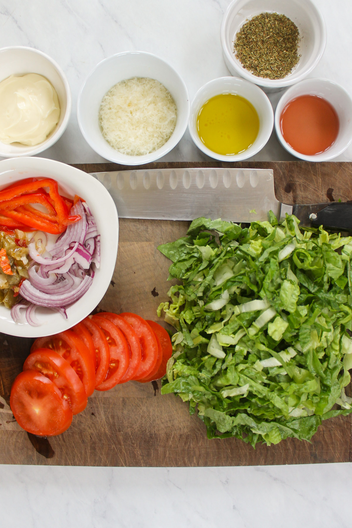Sliced tomato and lettuce on a cutting board with sliced peppers and onions.