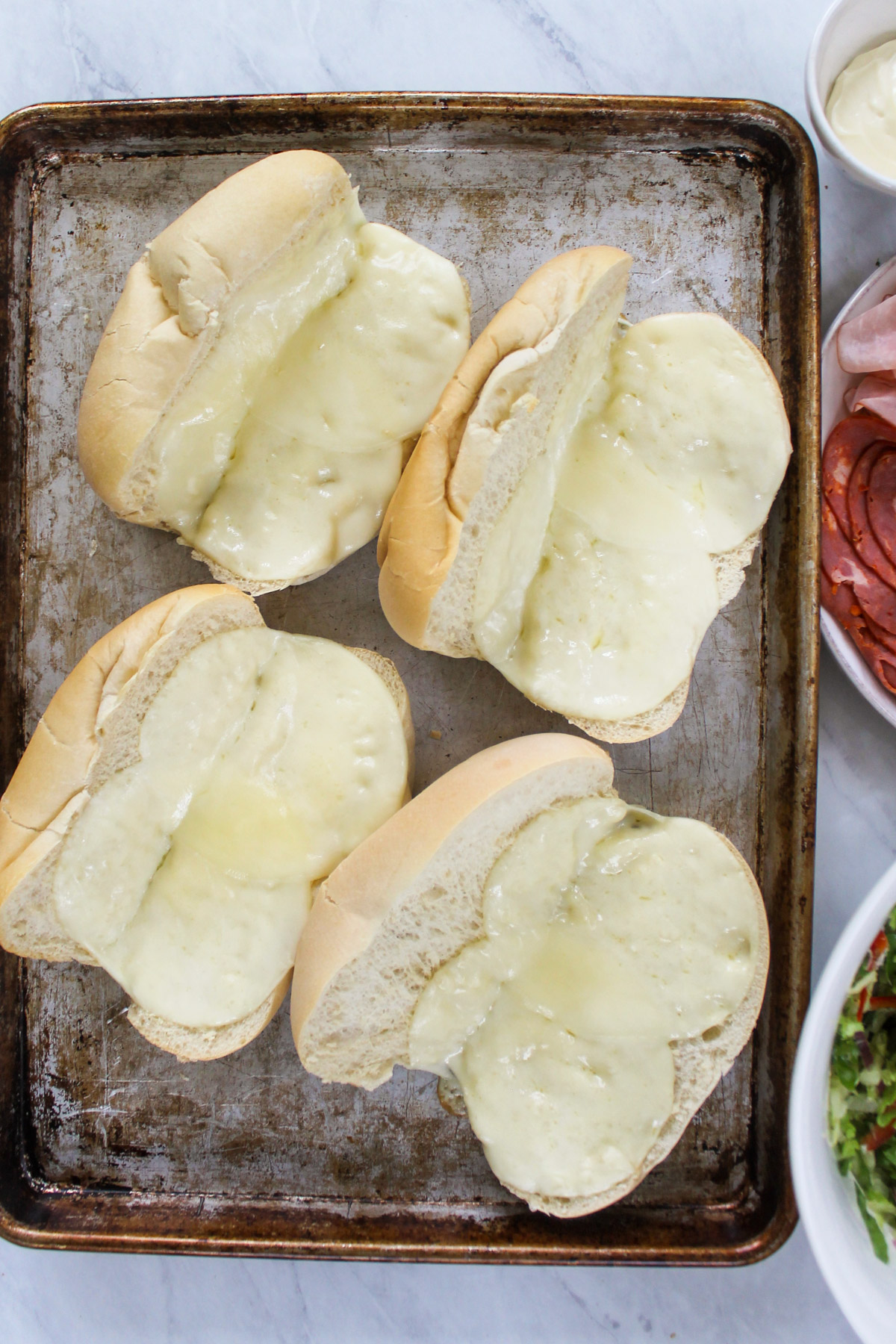 Toasted hoagie buns with melted provolone cheese on a sheet pan.