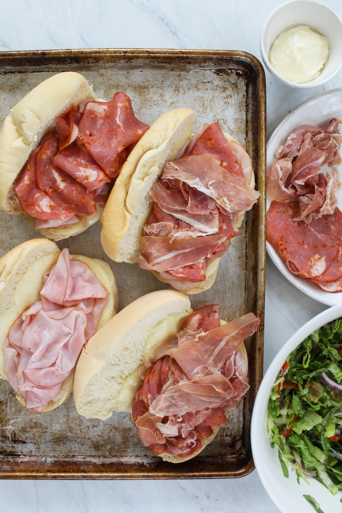 Italian deli meats including ham, Capicola and prosciutto are piled onto toasted hoagie buns.