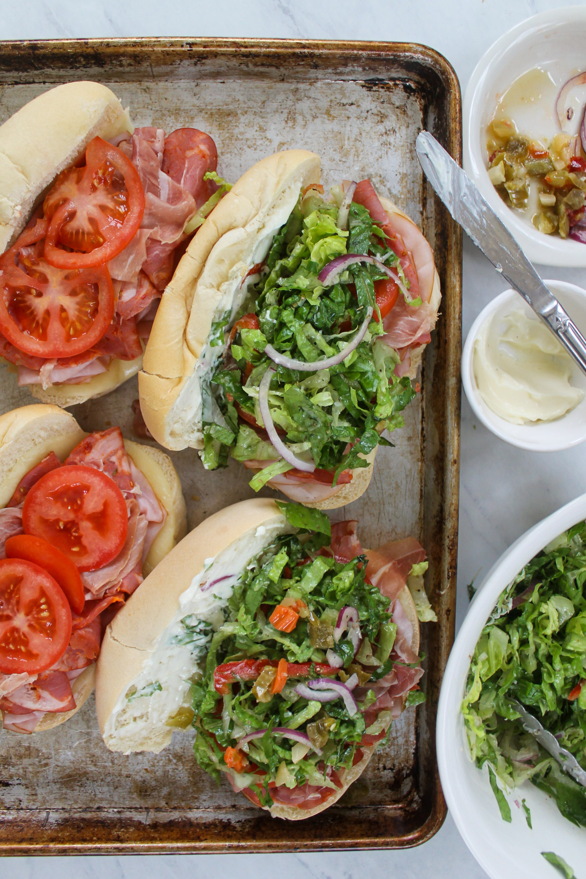 Sliced tomato and dressed lettuce piled onto grinder sandwiches.