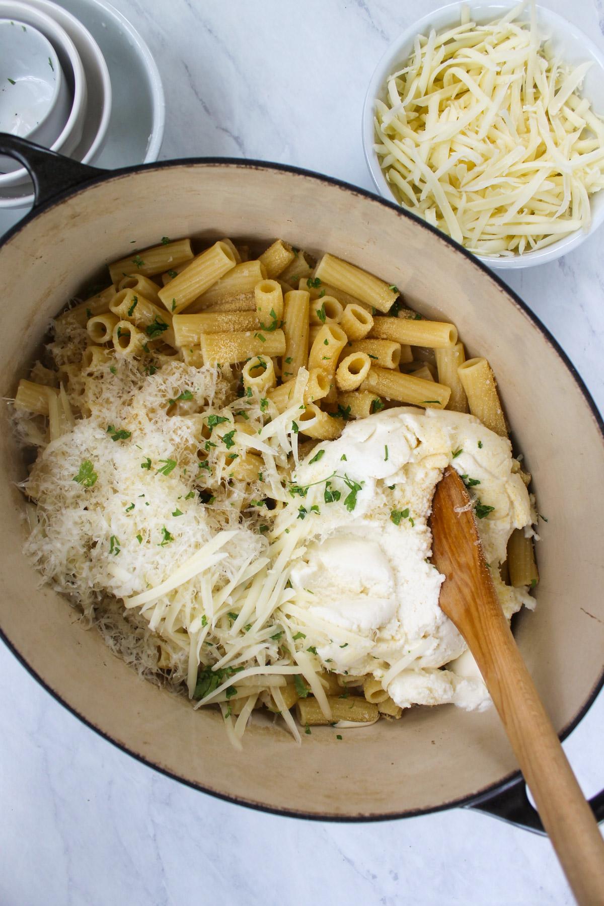 A pot of cooked rigatoni pasta being mixed with ricotta and shredded cheeses.