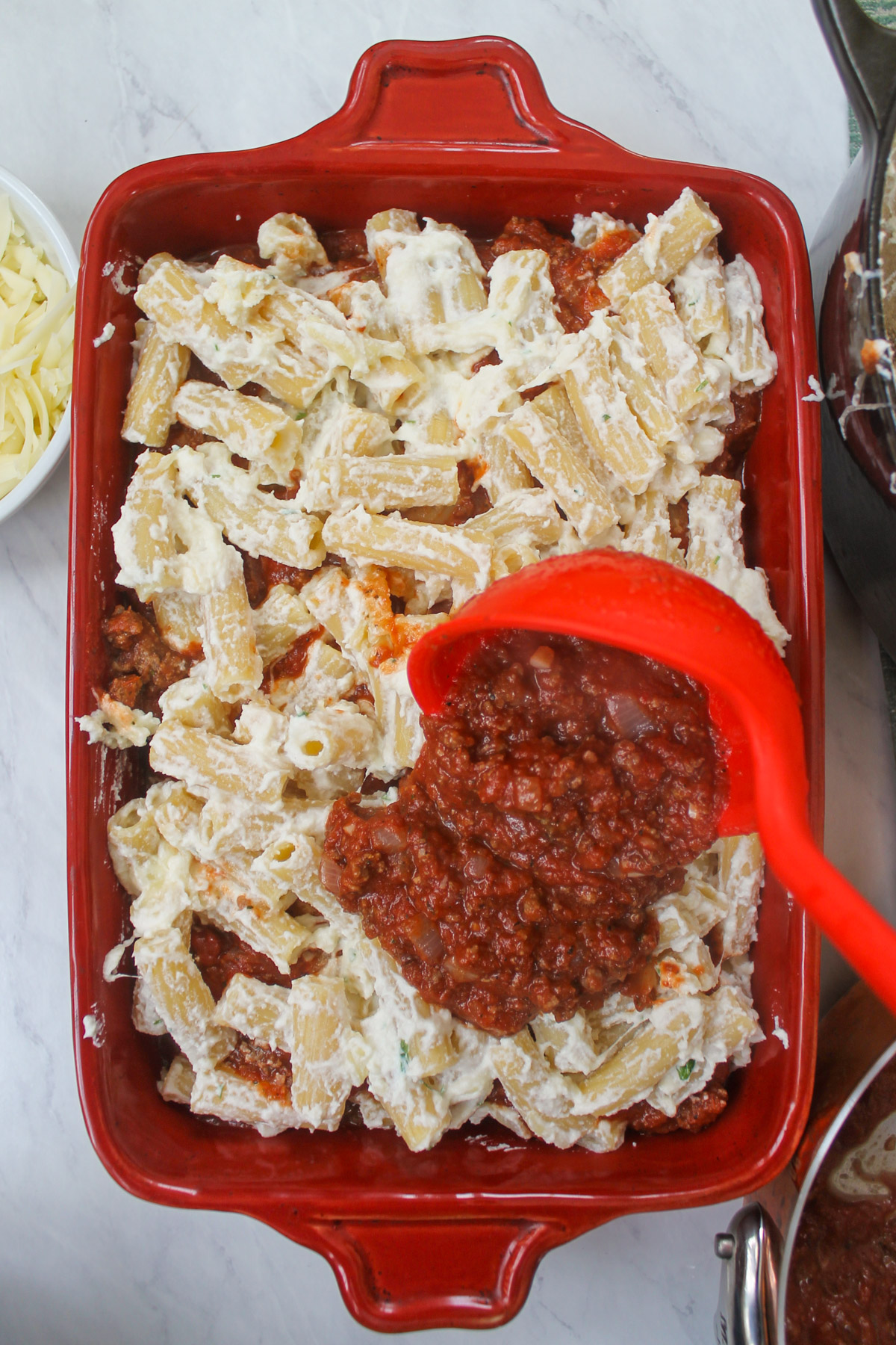 Layering a baking dish with tomato sauce and ricotta pasta.