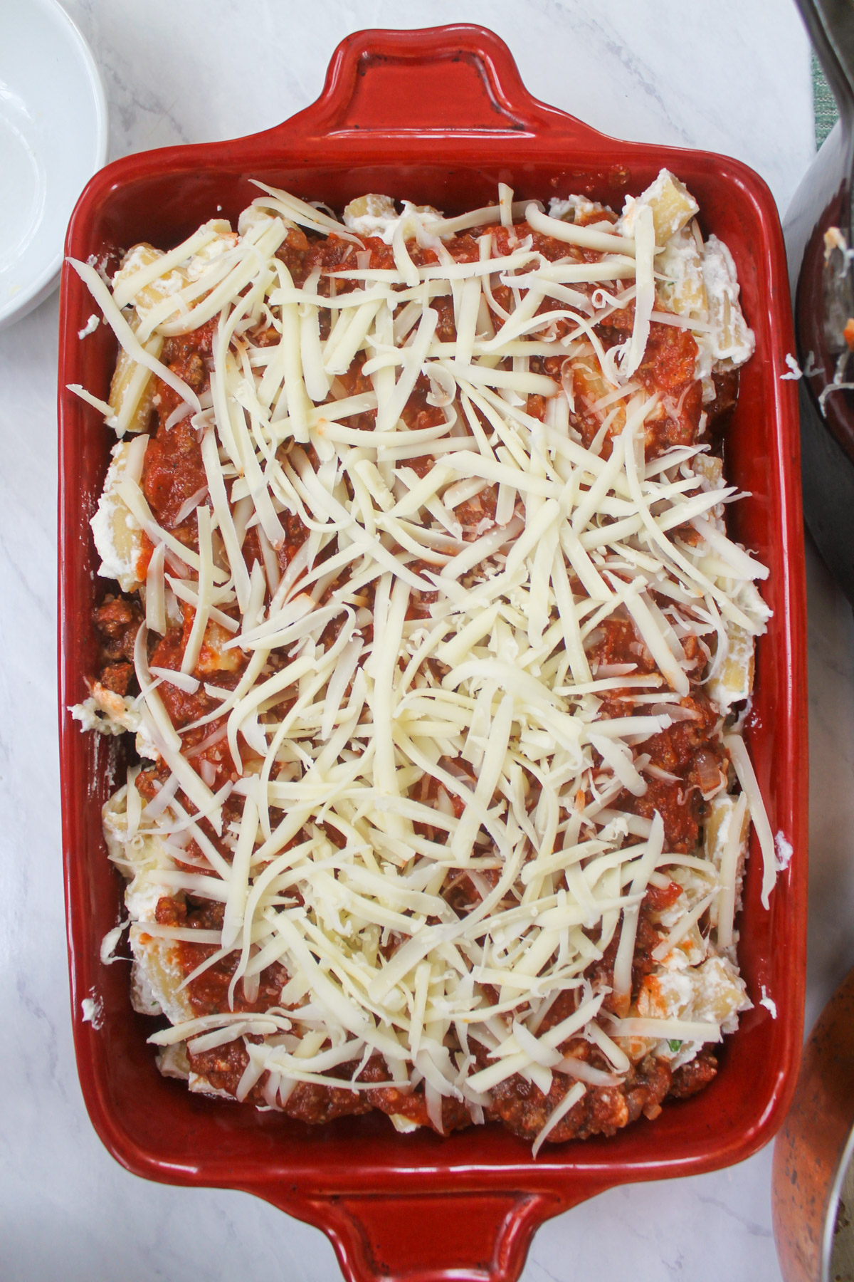 Rigatoni pasta bake topped with shredded cheese ready to be baked.