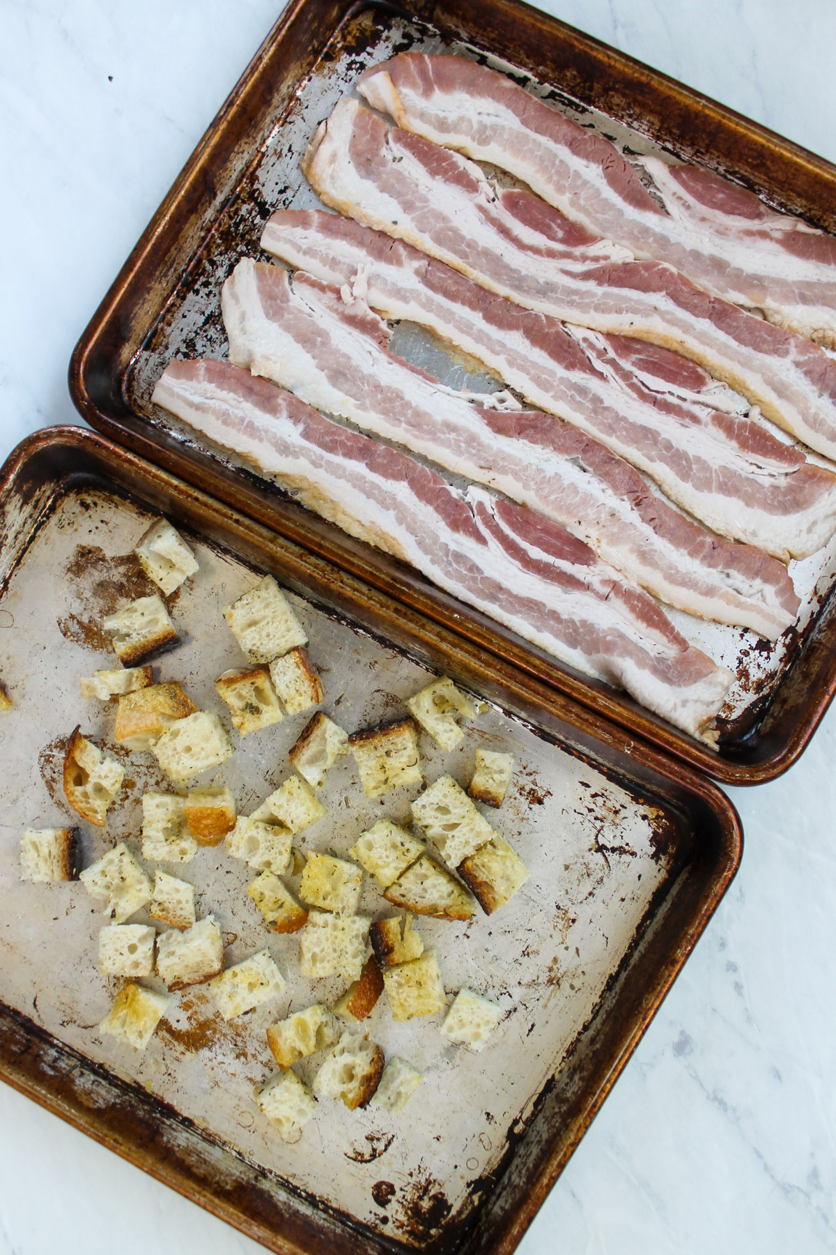 Raw bacon on a sheet pan and bread cubes for croutons.