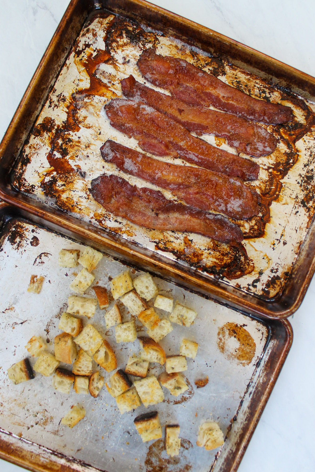 A sheet pan of cooked baked and a pan of homemade croutons.