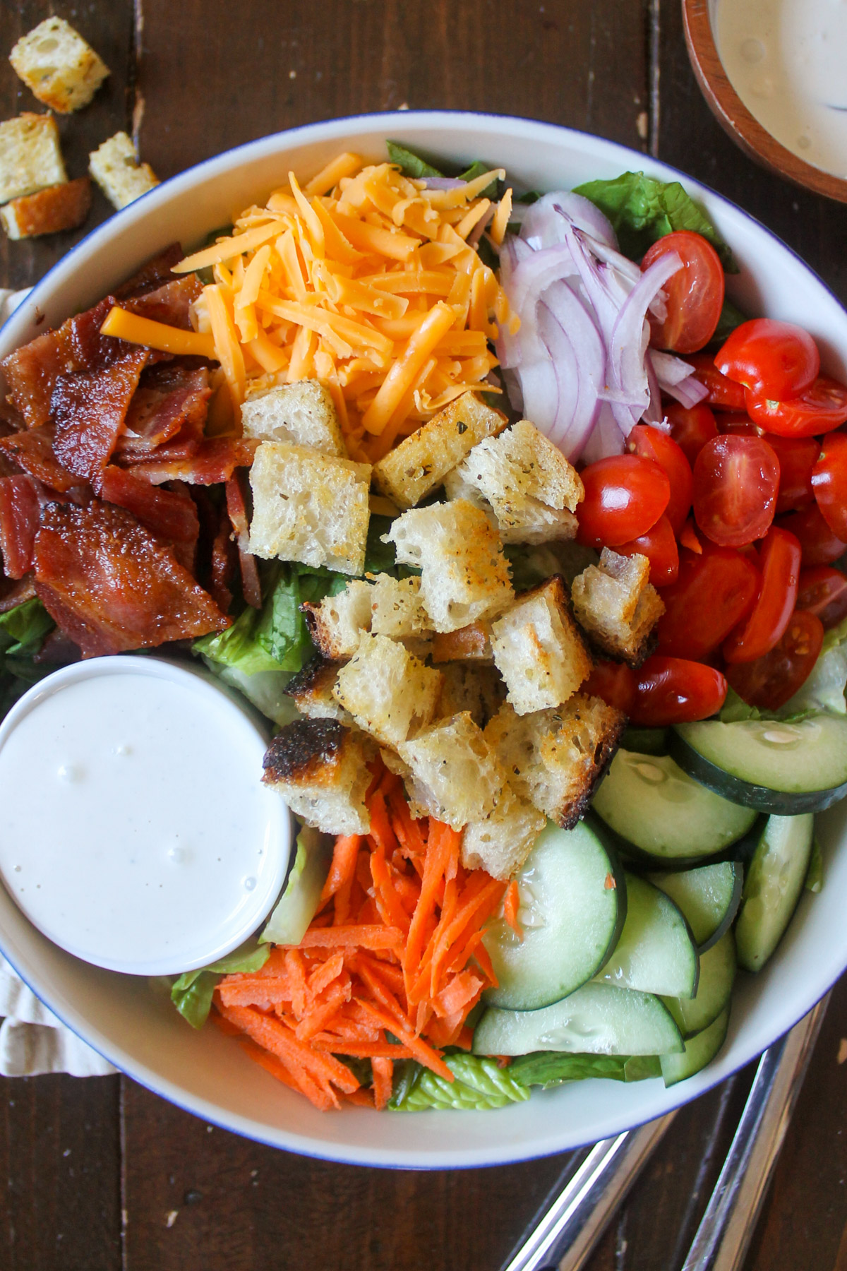 Bacon, cheese, onion, tomato, cucumber, carrot, croutons and dressing on a salad.