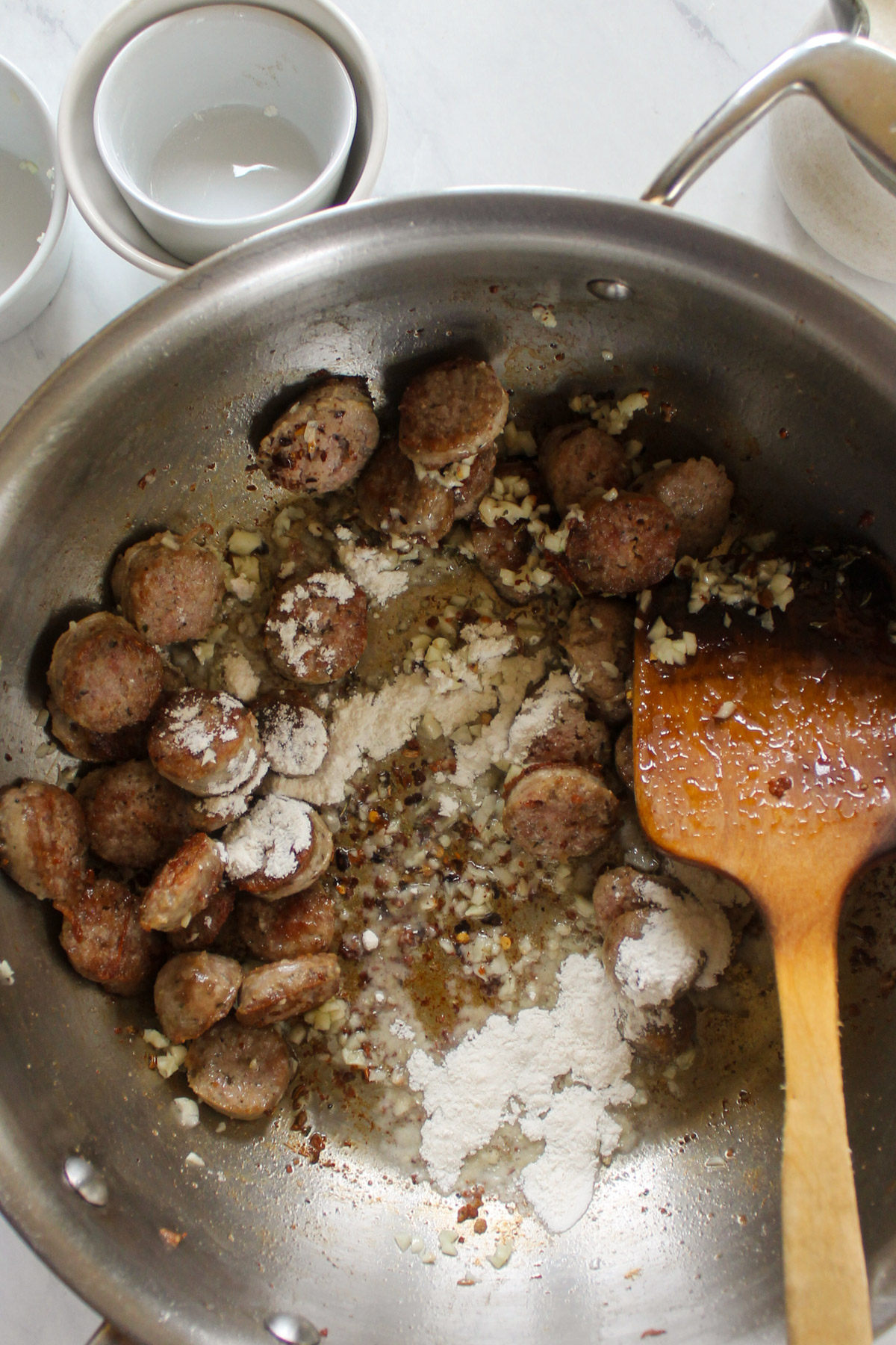 Adding garlic and flour to browned Italian sausage in a skillet.