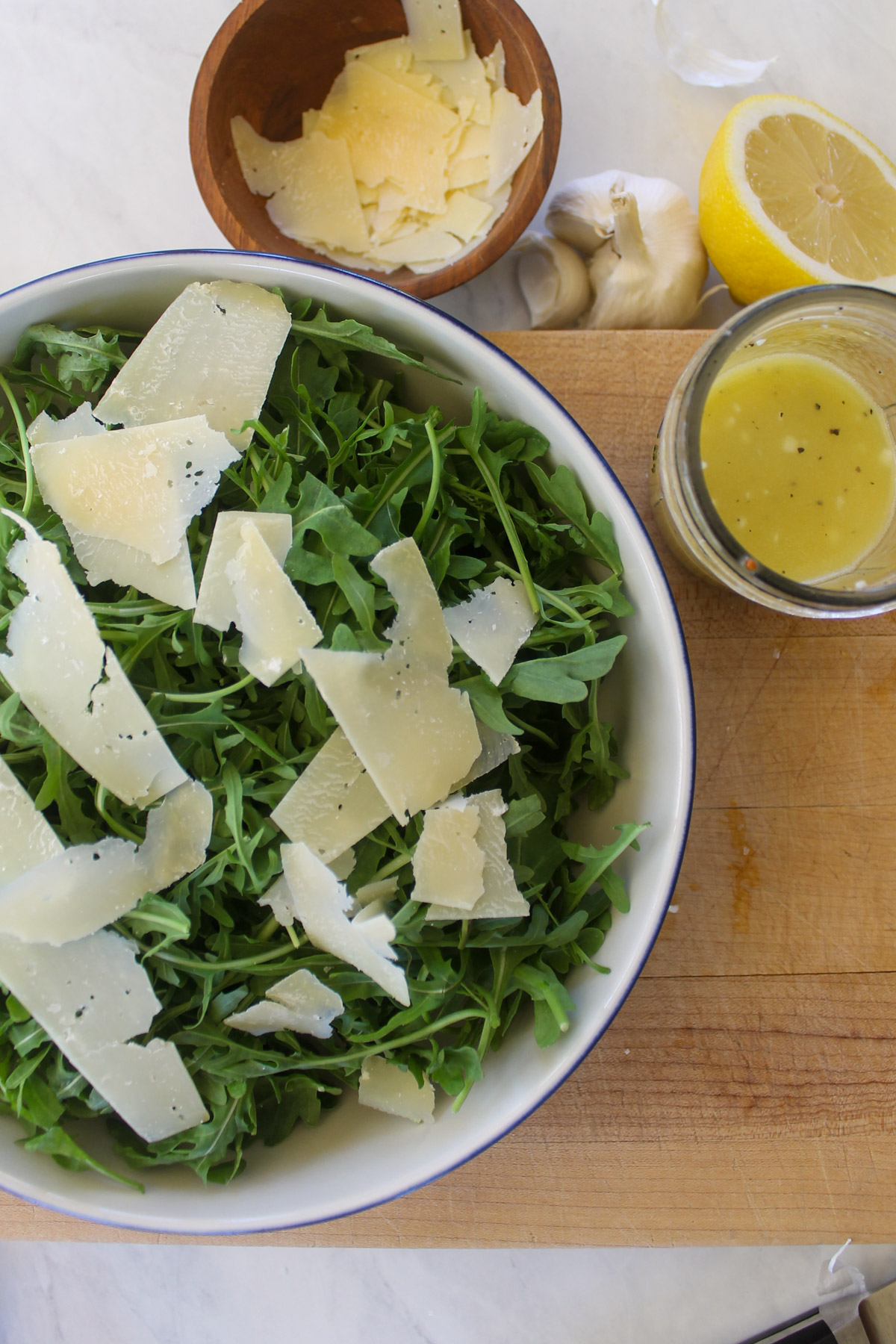 Assembling an arugula salad with shaved Parmesan cheese and lemon dressing.