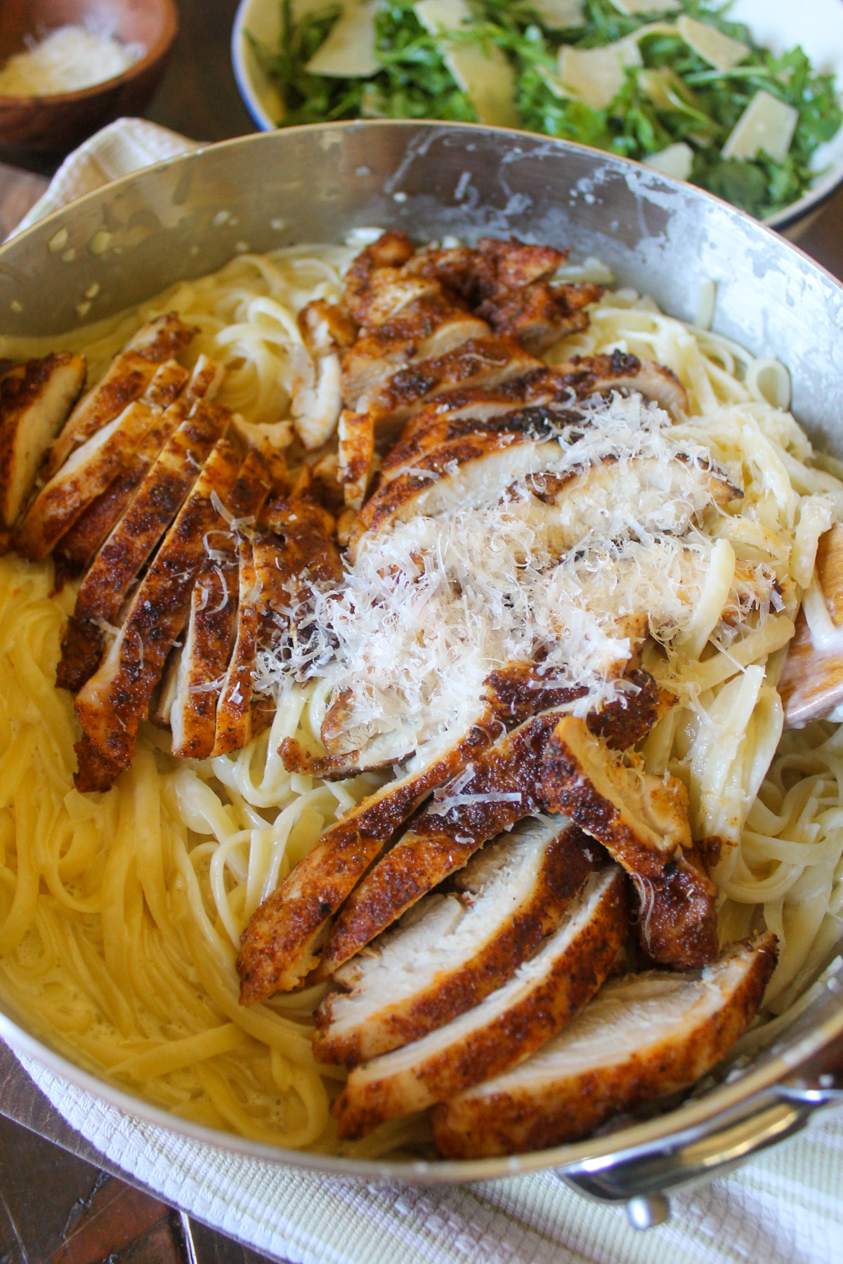 Cream sauce pasta topped with sliced blackened chicken and a salad.