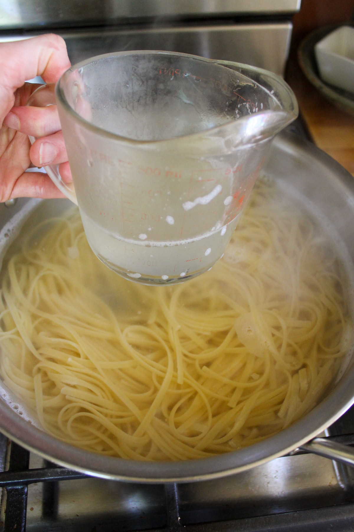 Using a glass measuring cup to reserve pasta water from boiling linguine.