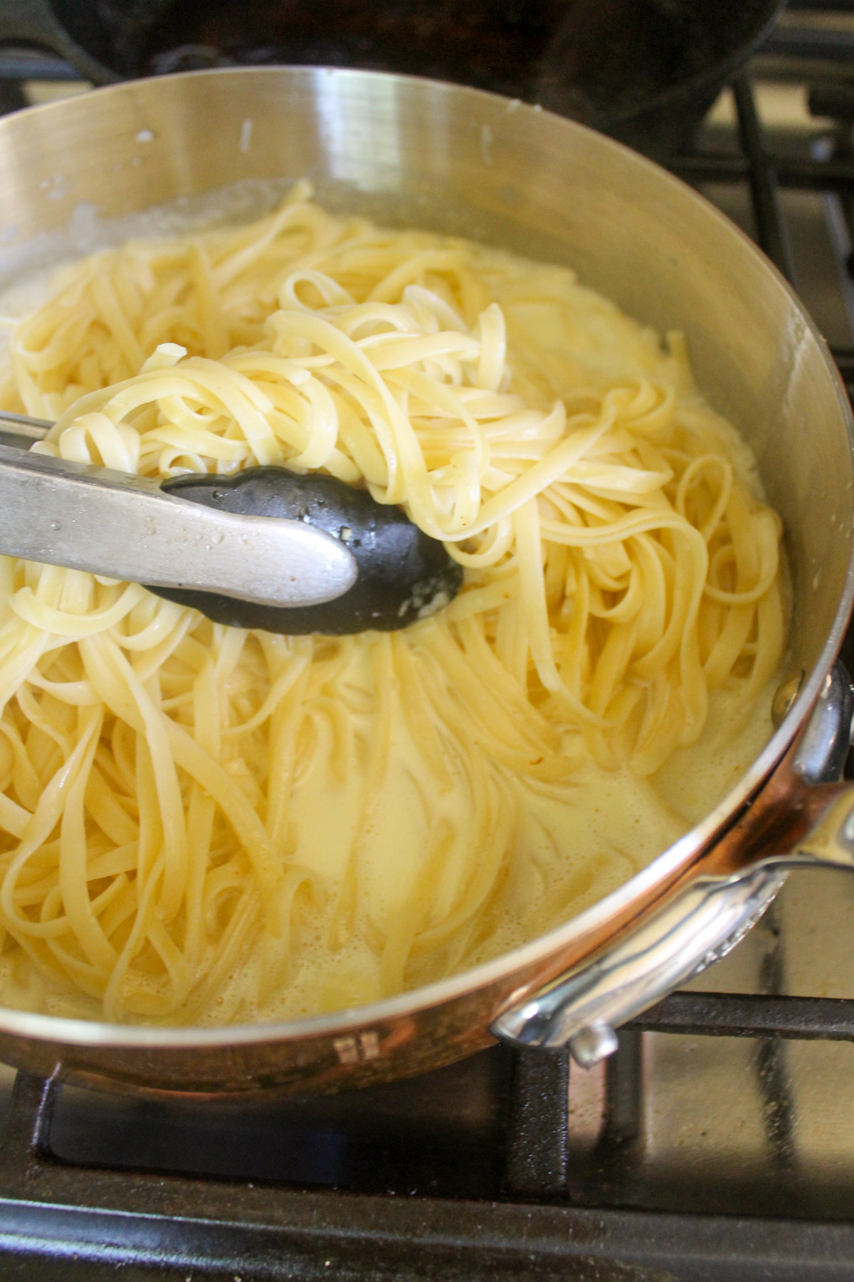 Using tongs to toss linguine pasta with cream sauce.