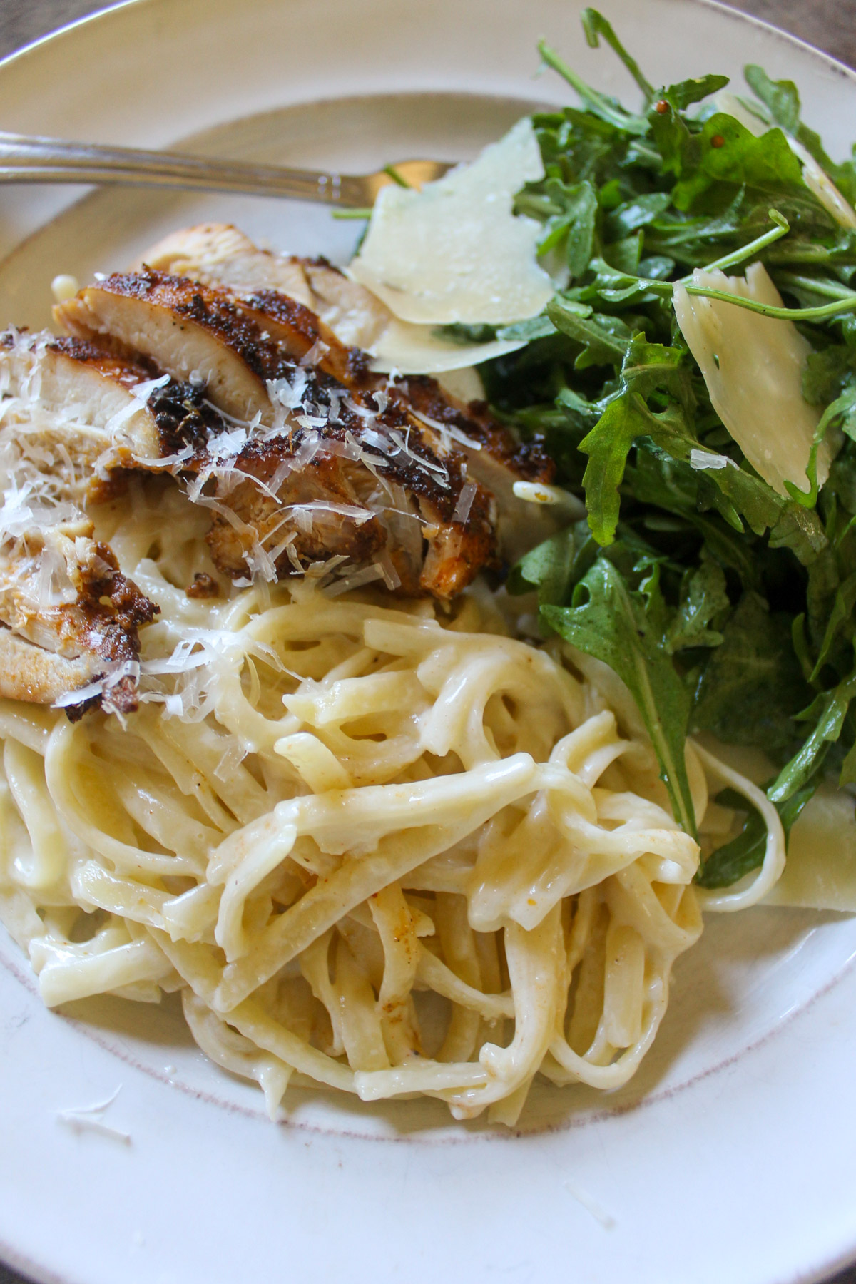 A plate of Alfredo linguine pasta with blackened chicken and salad.