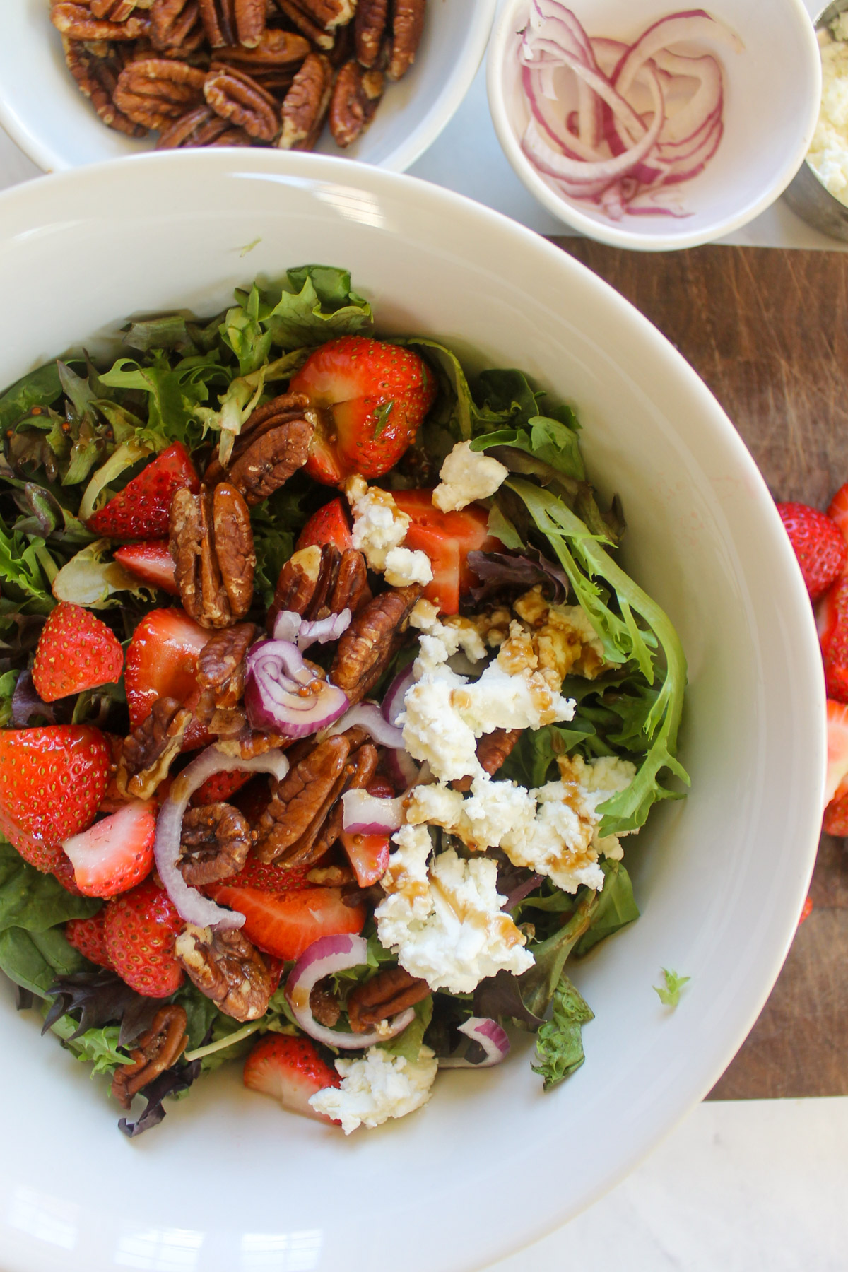 Adding strawberries, goat cheese, red onion and pecans to a bowl of lettuce.