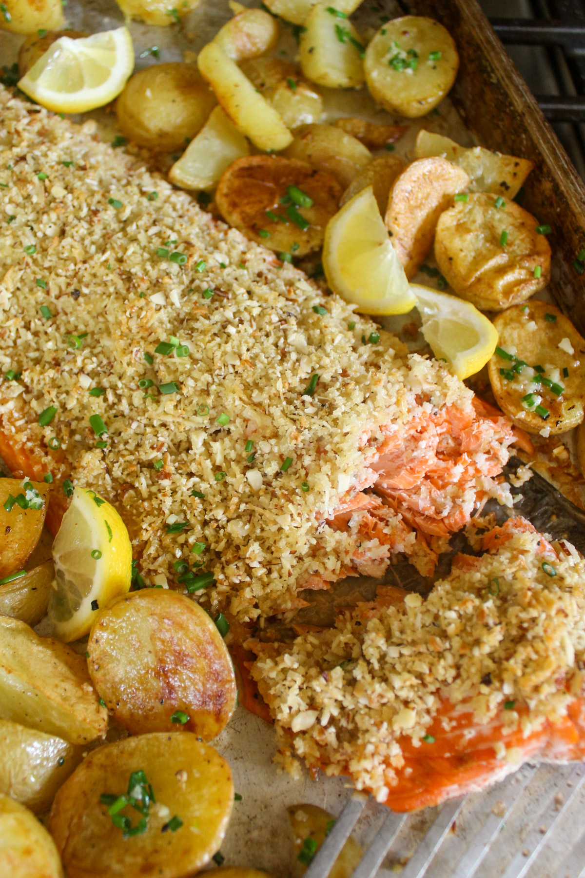 An almond crusted filet of salmon with crispy potatoes on a sheet pan with lemon.