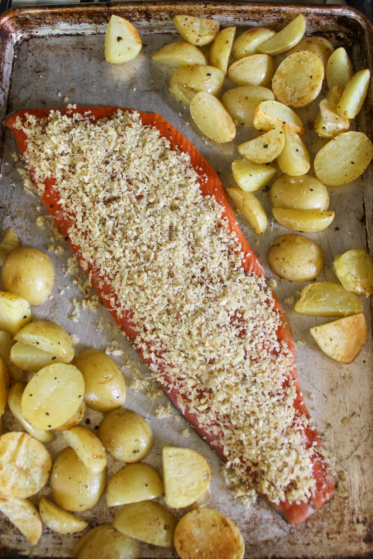 Almond crust topping added to a raw salmon filet on a sheet pan with potatoes.