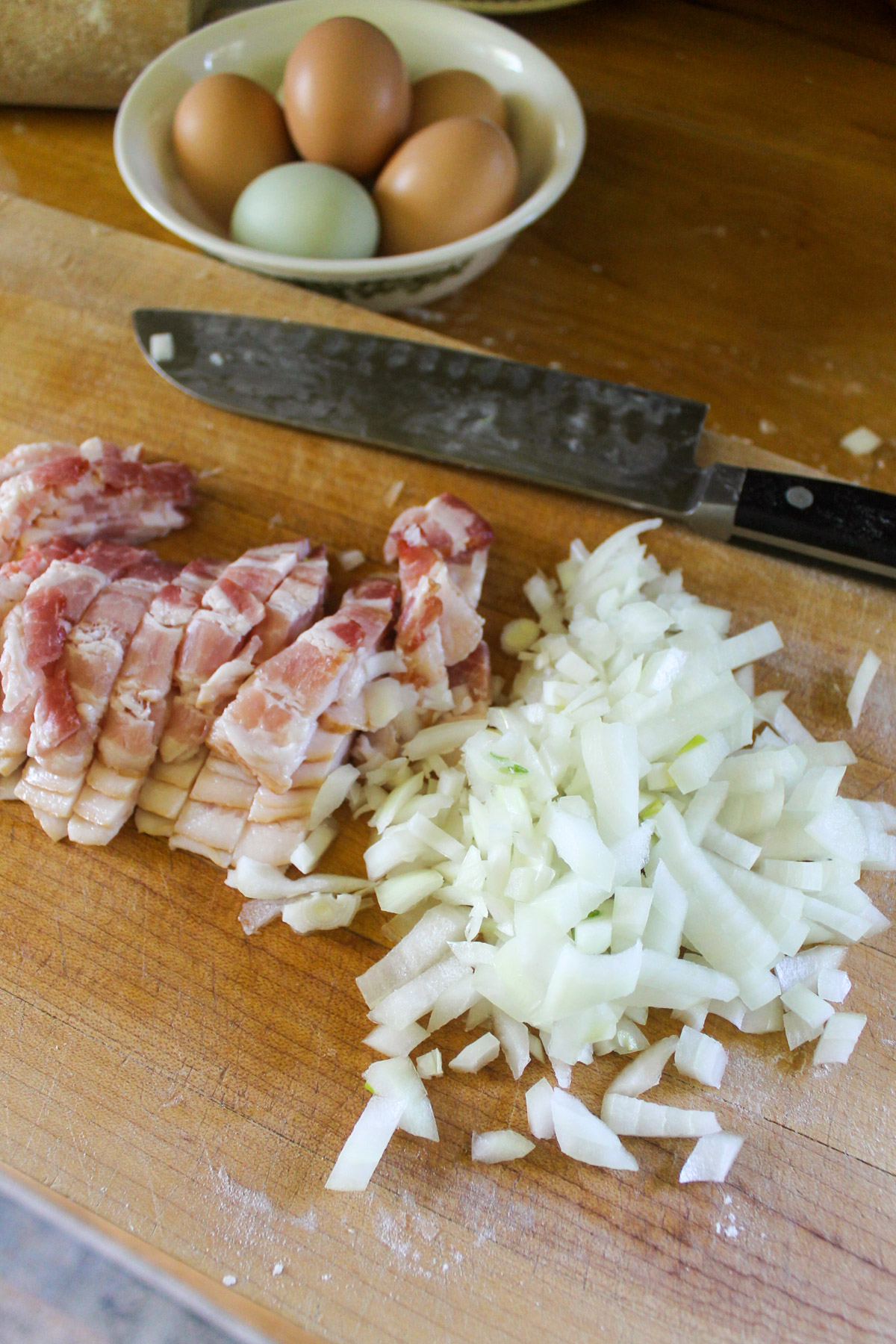 Raw bacon and onion chopped on a cutting board.