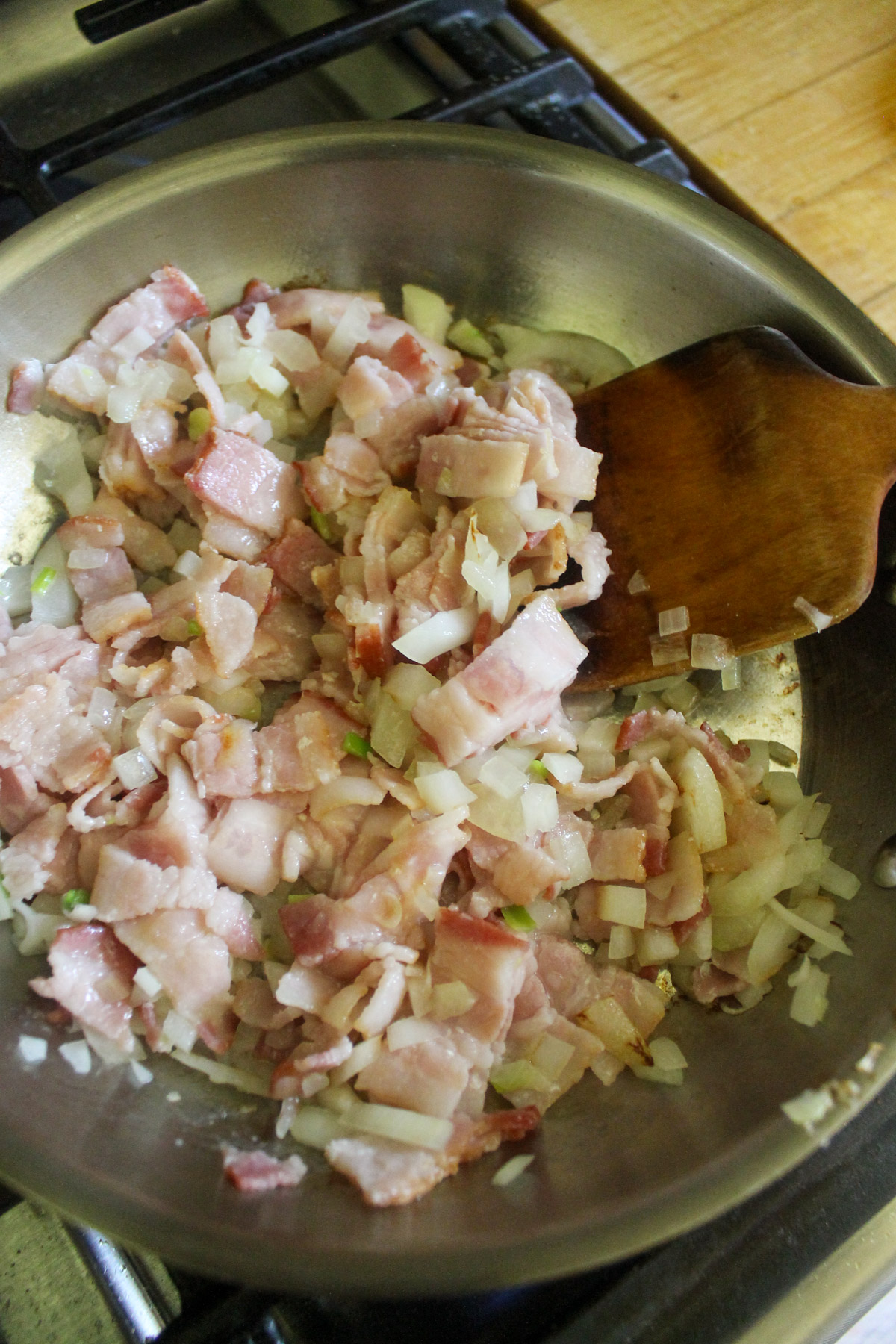 Raw bacon and onions starting to cook in a skillet.