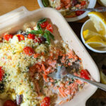 A baking dish of salmon coated in breadcrumbs with tomatoes and olives.