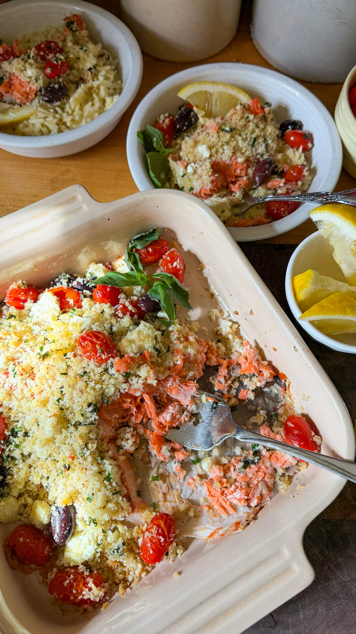 A baking dish of panko coated baked salmon with tomato, olives and feta.