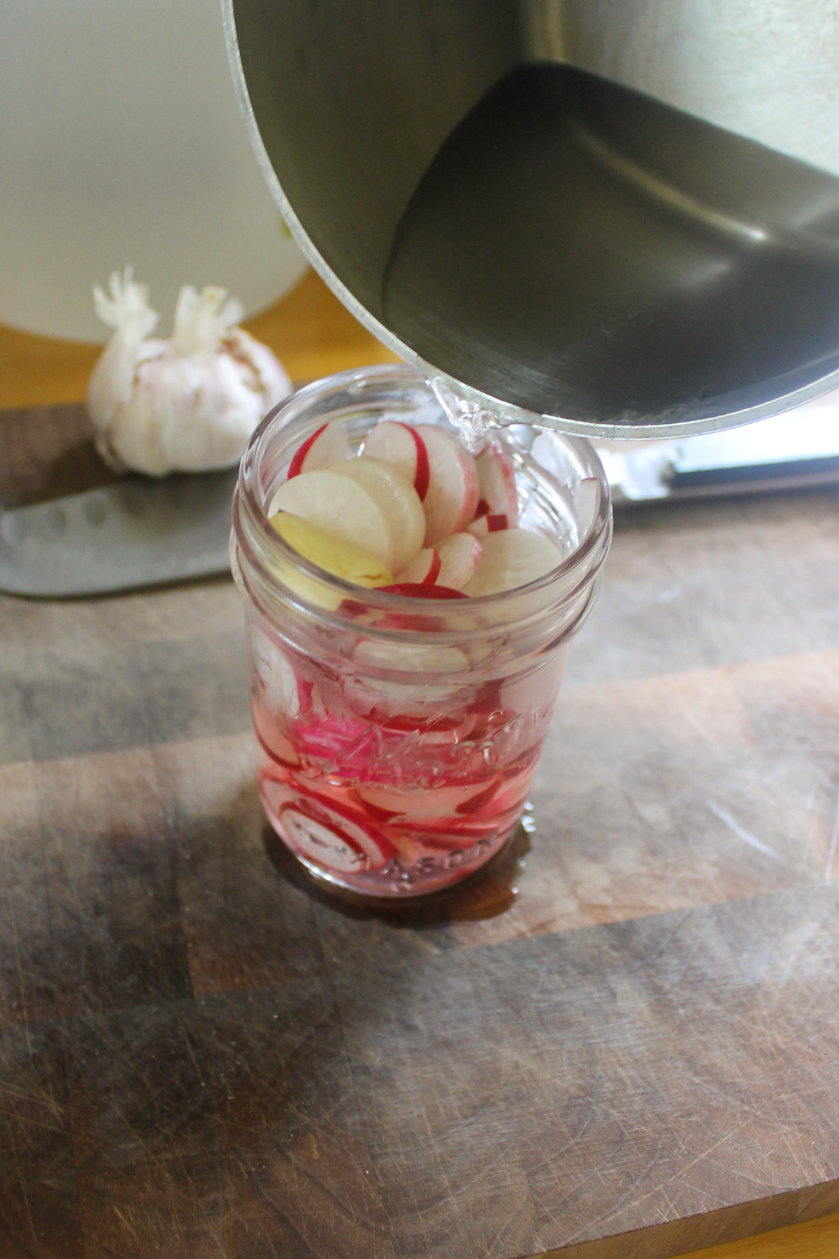 Pouring brine from a pot over a jar of sliced radish.