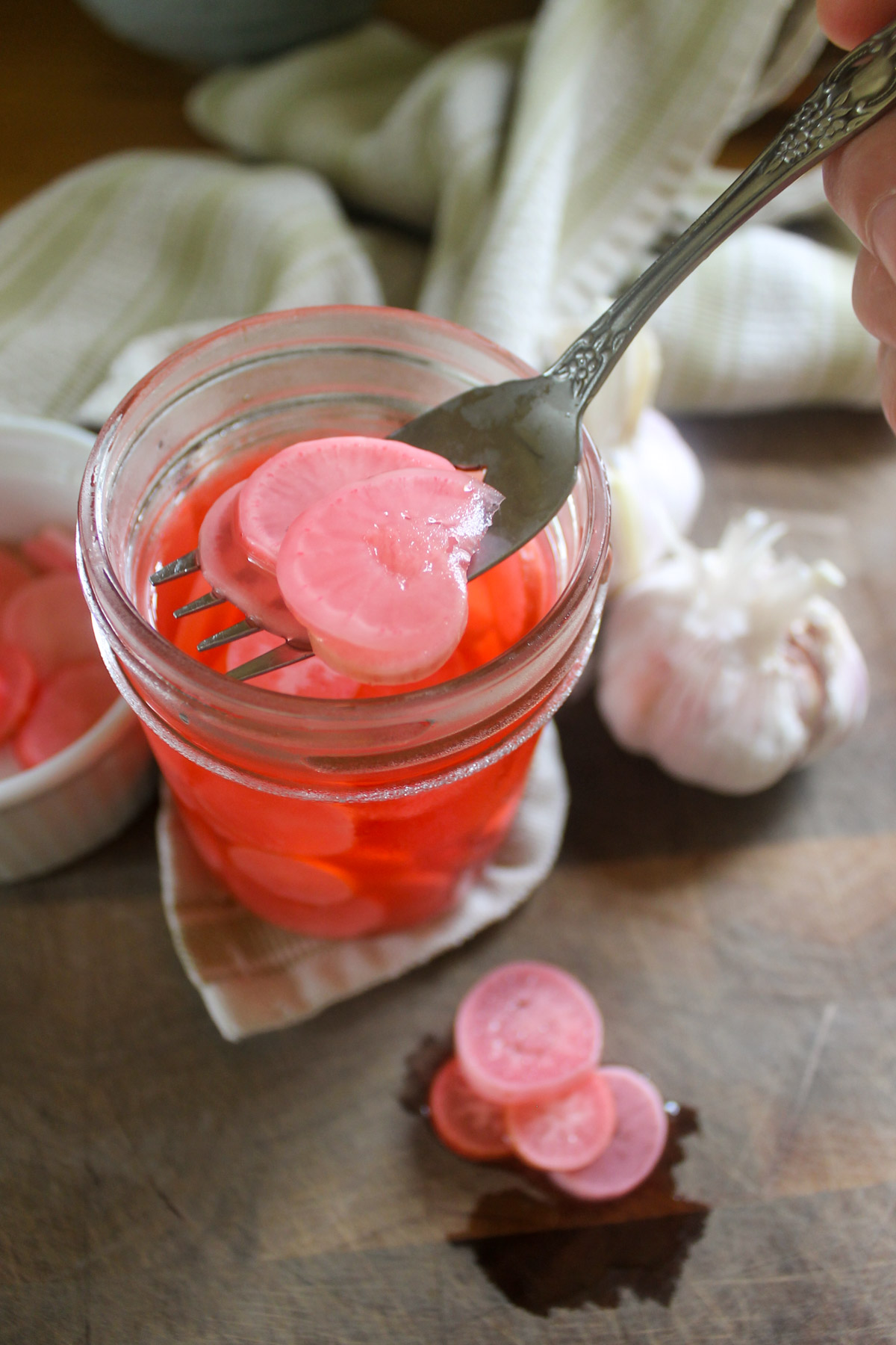 A fork scooping pickled radishes from a jar.
