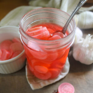 A jar of pickled radishes in pink brine.