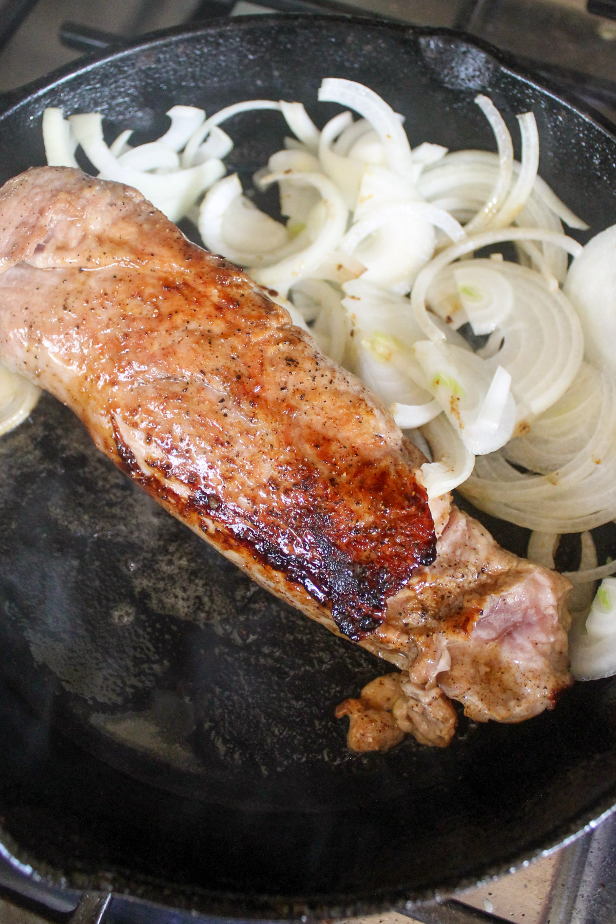 Seared pork tenderloin with sliced onions in a skillet.