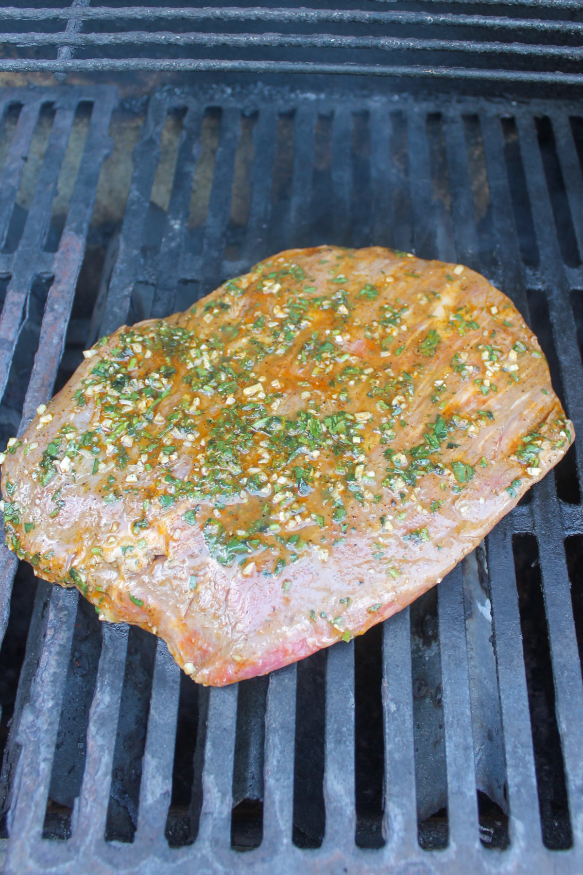 The marinaded flank steak on an outdoor grill.