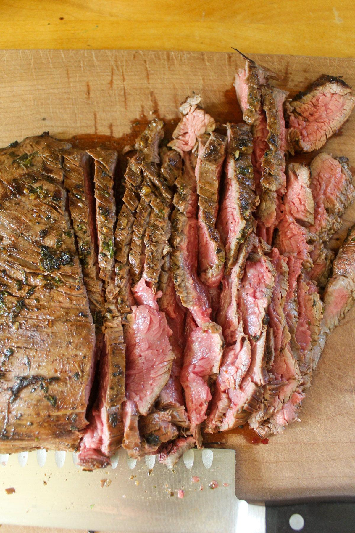 Slicing medium rare flank steak on a cutting board.