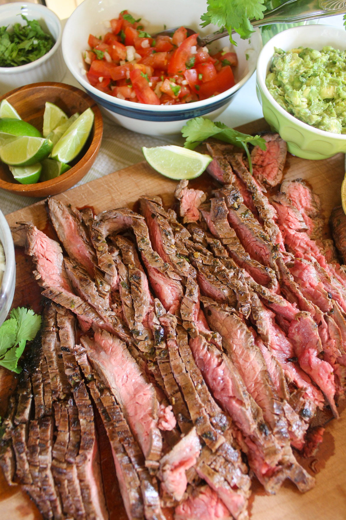 Sliced flank steak on a cutting board with taco toppings.