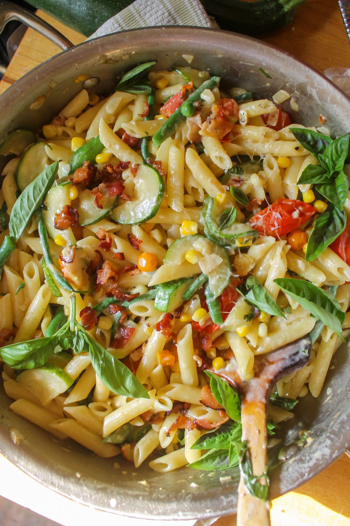 Garden harvest pasta in a skillet with bacon and basil.