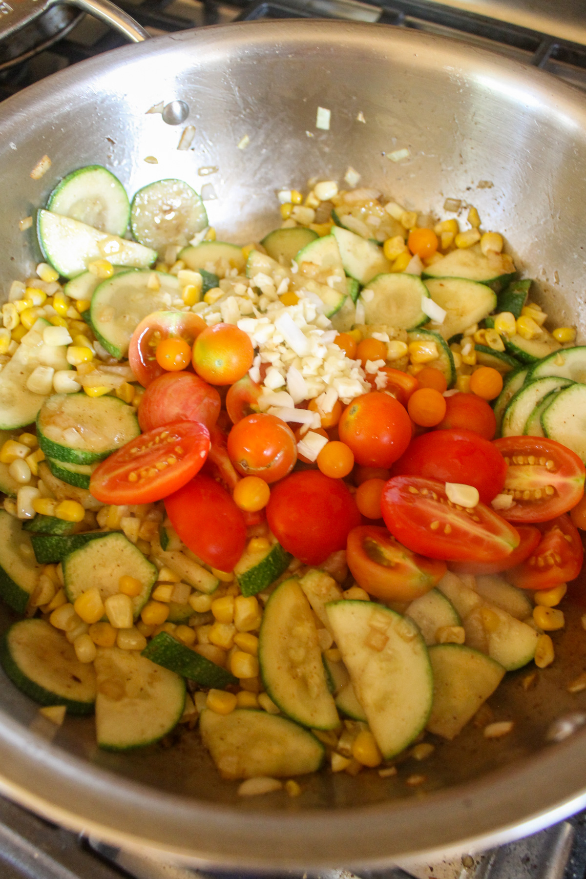 Adding corn, fresh tomatoes and garlic to zucchini in a skillet.