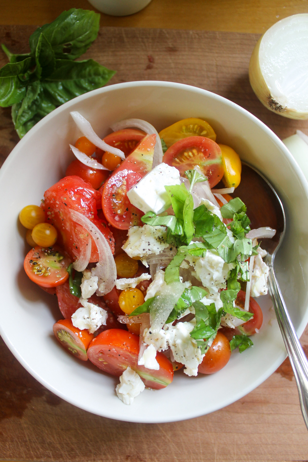 Tomatoes, onions, feta, and basil in a bowl.