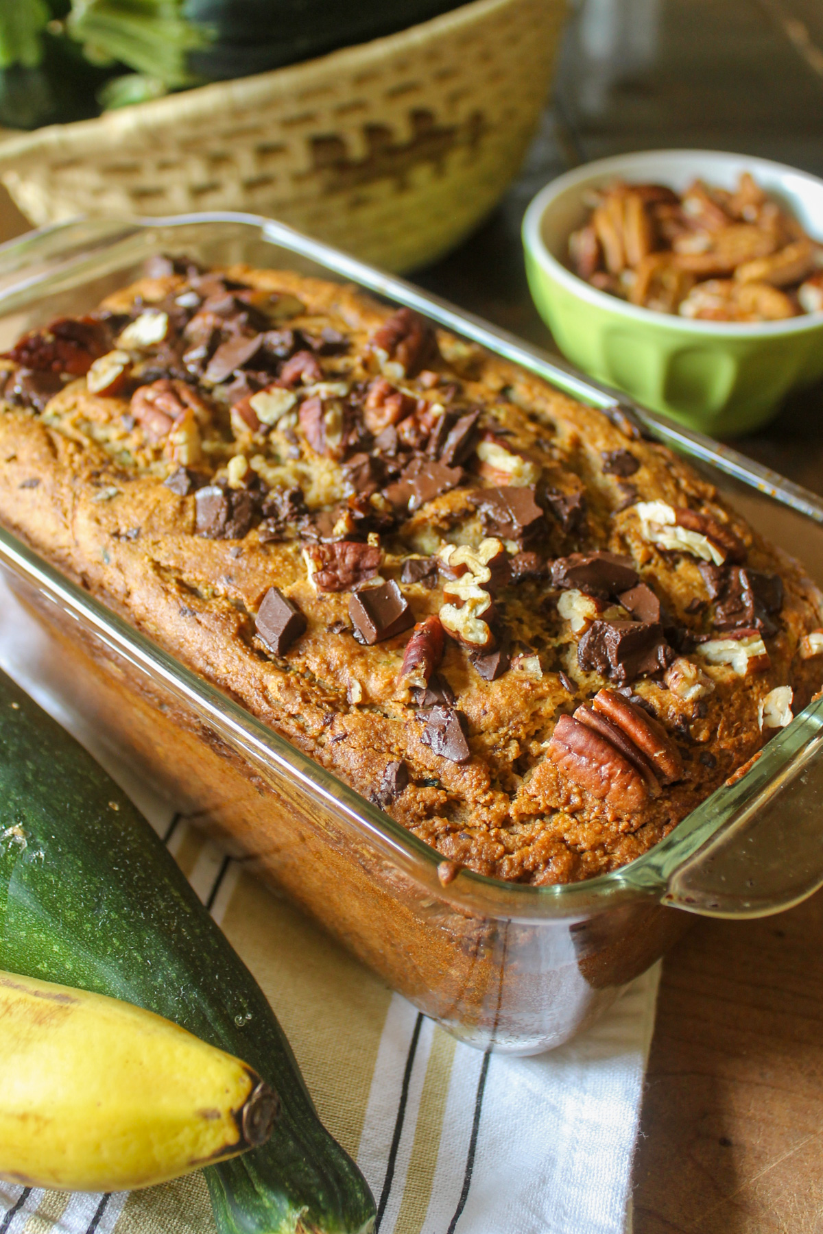 A loaf of zucchini banana bread on a table with zucchini.