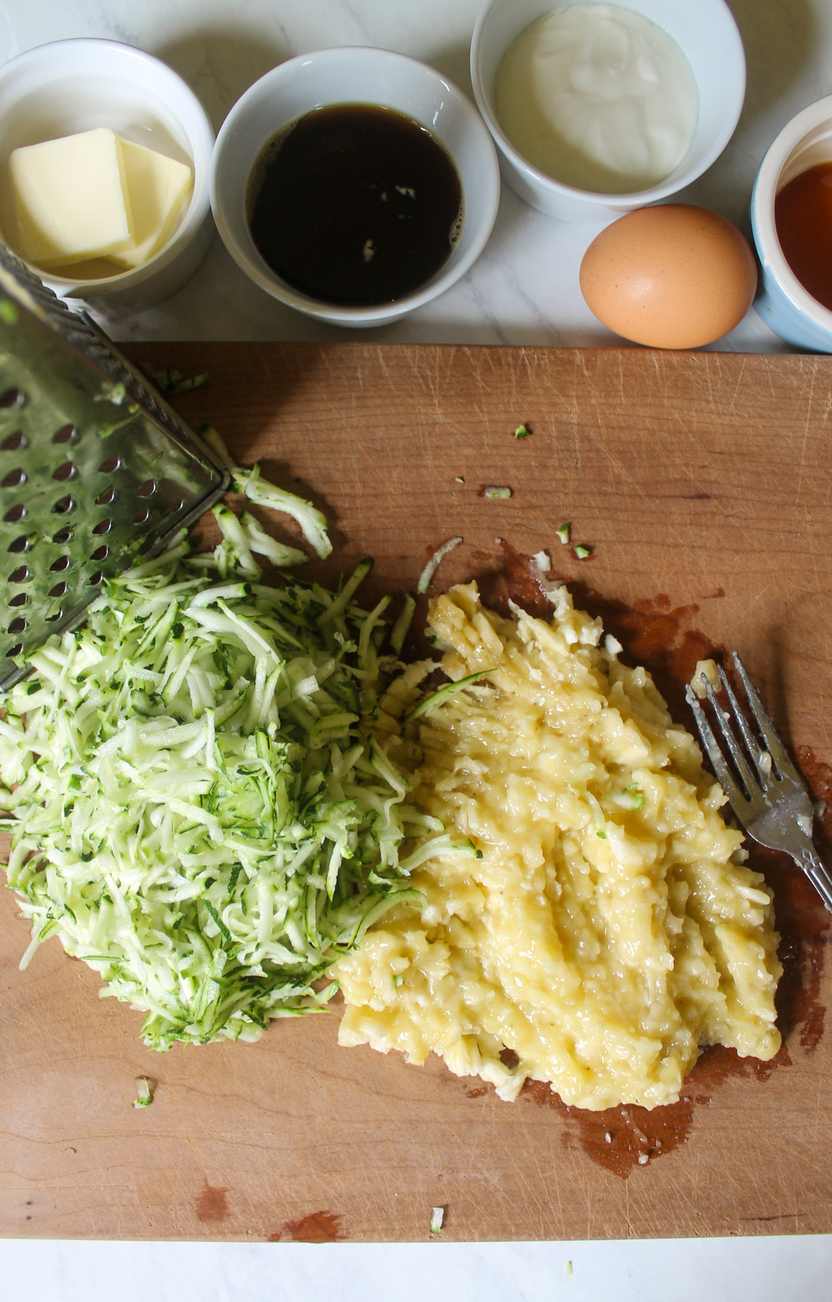 Mashed bananas and shredded zucchini on a cutting board.