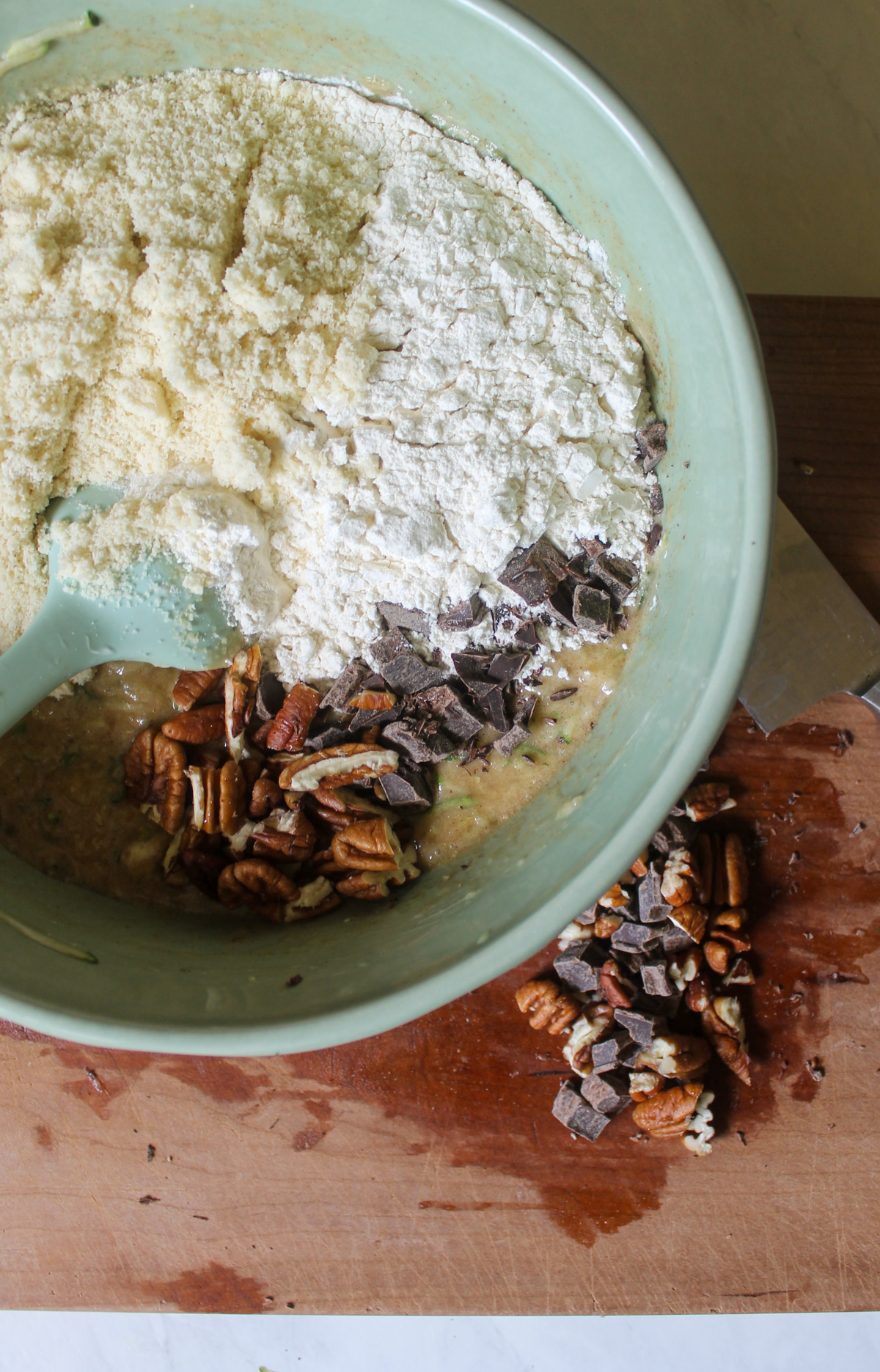 Adding dry ingredients and chopped pecans and chocolate chunks to zucchini bread batter.