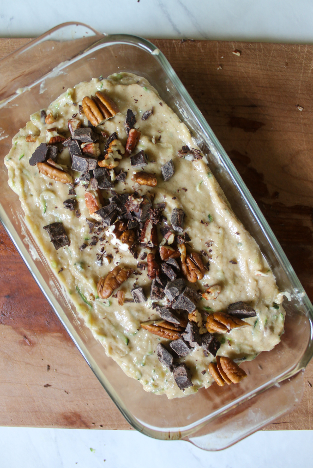 Zucchini Banana Bread batter in a loaf pan topped with chopped nuts and chocolate.
