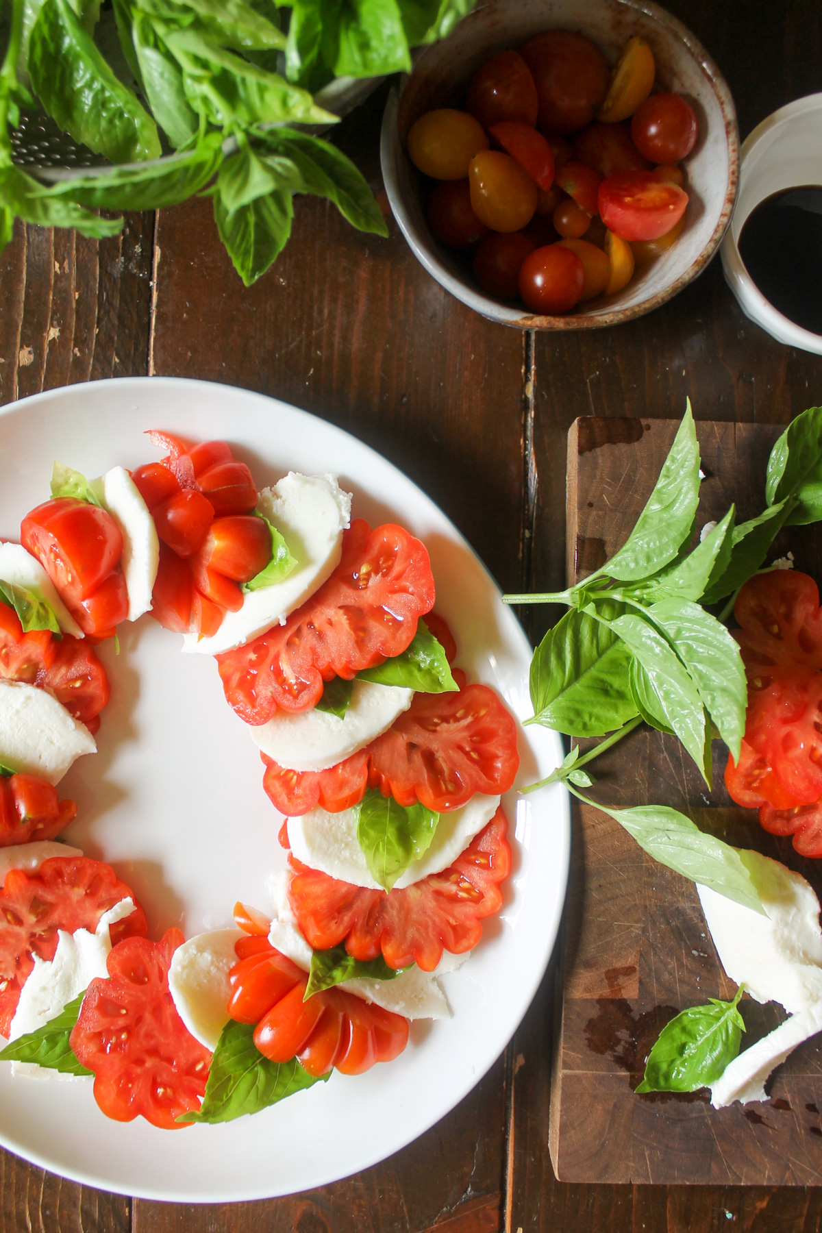 Layering caprese salad on a plate with sliced tomato, mozzarella cheese and fresh basil leaves.