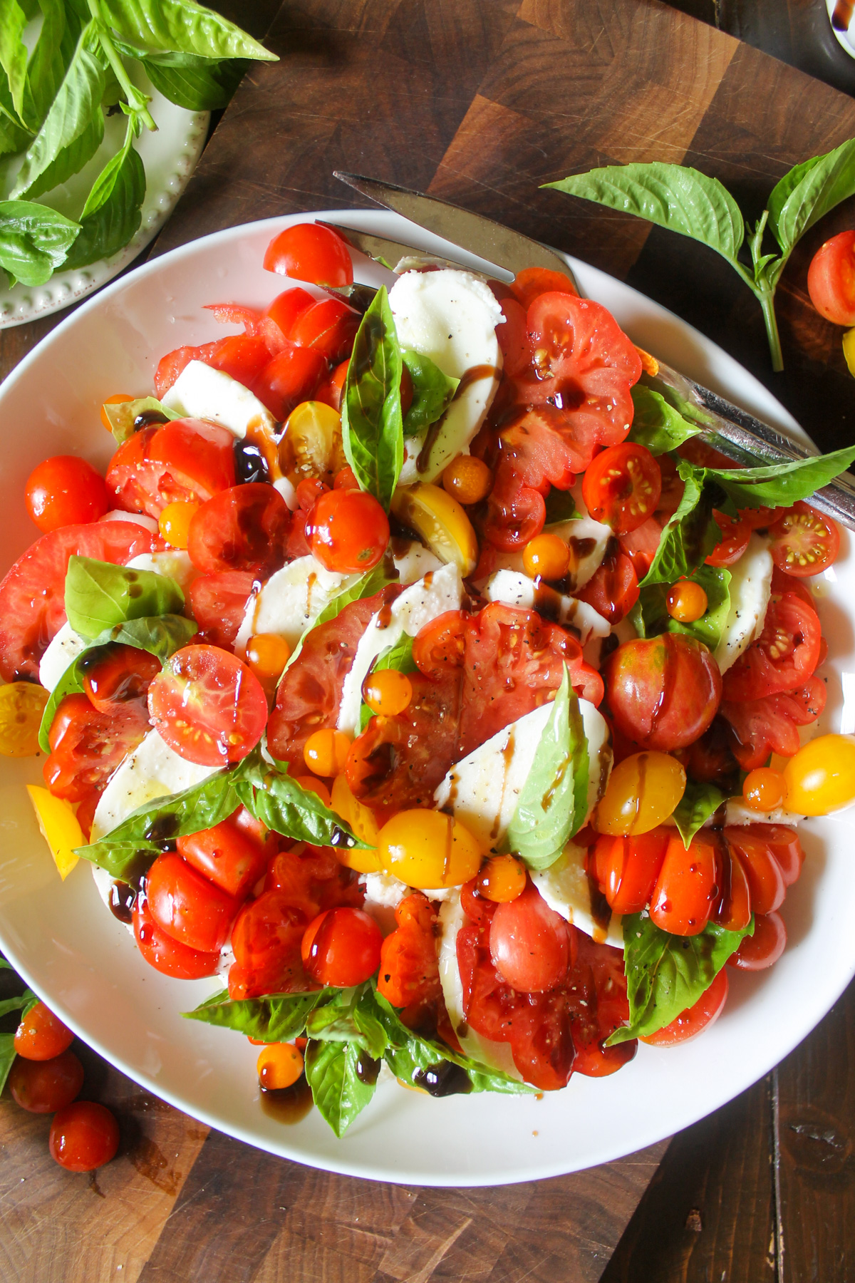 A plate of caprese salad with red and yellow tomatoes, basil and mozzarella cheese.