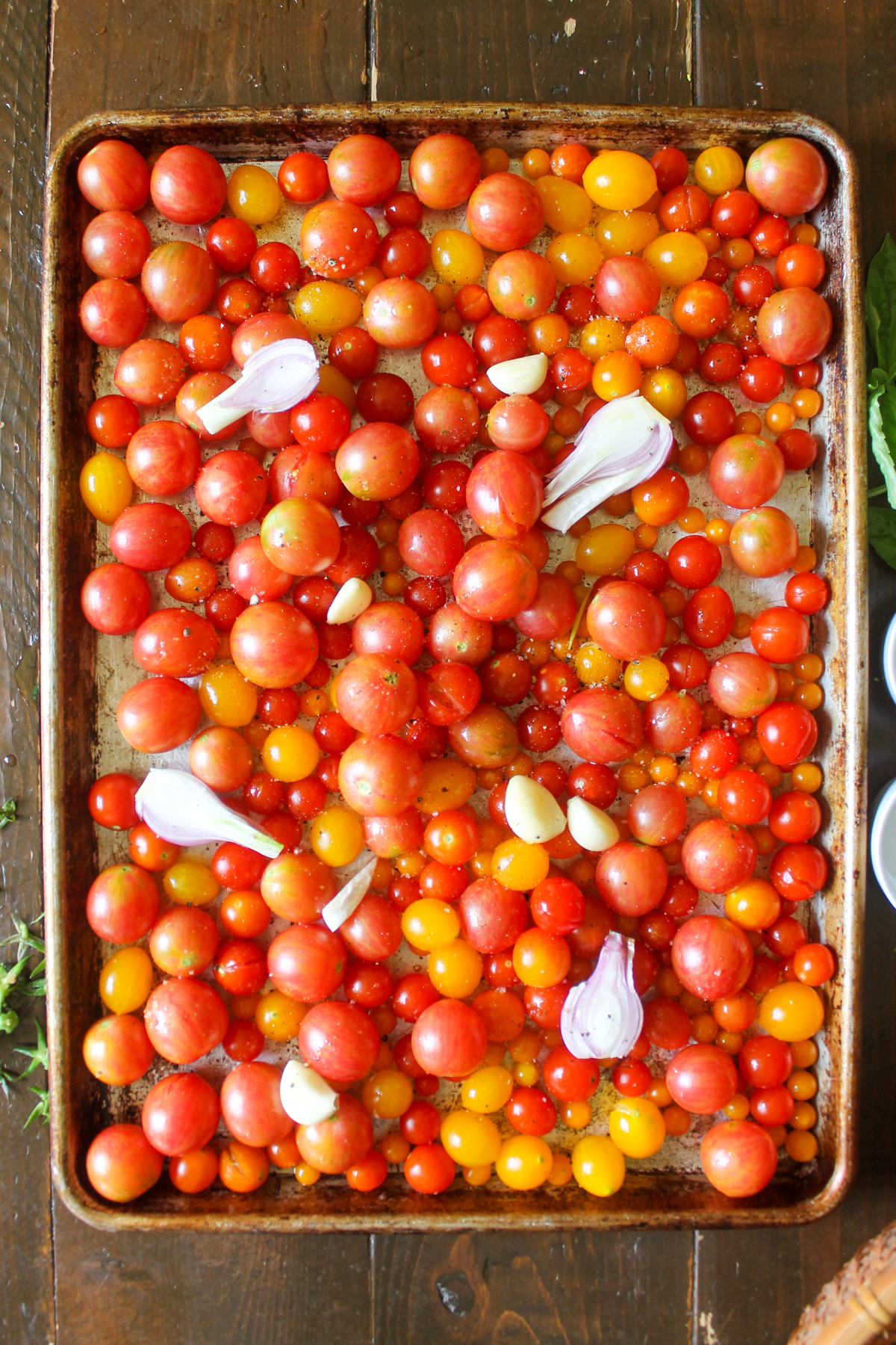 Cherry tomatoes with onions and garlic on a sheet pan ready to roast.