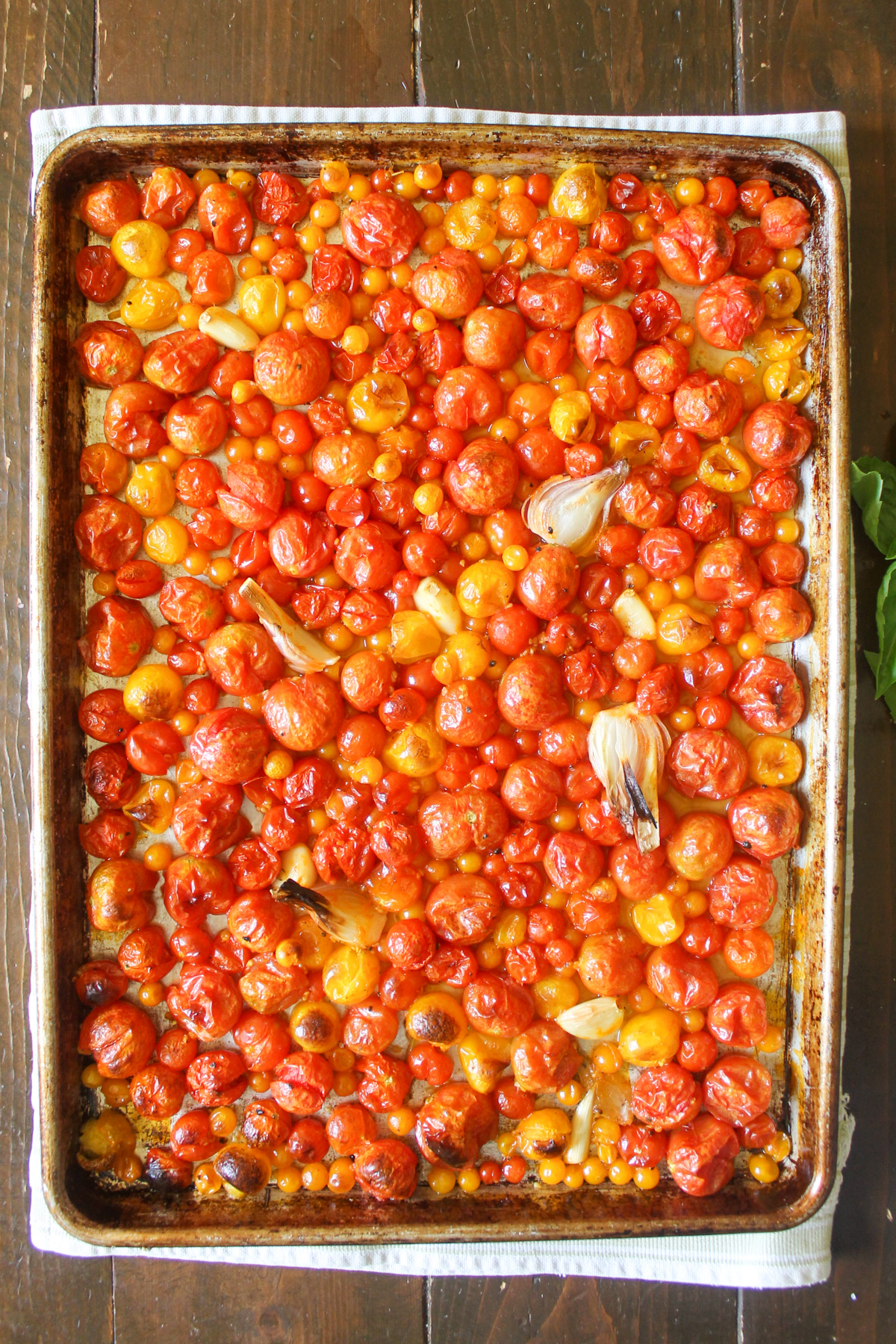 Roasted cherry tomatoes with onions and garlic on a sheet pan.