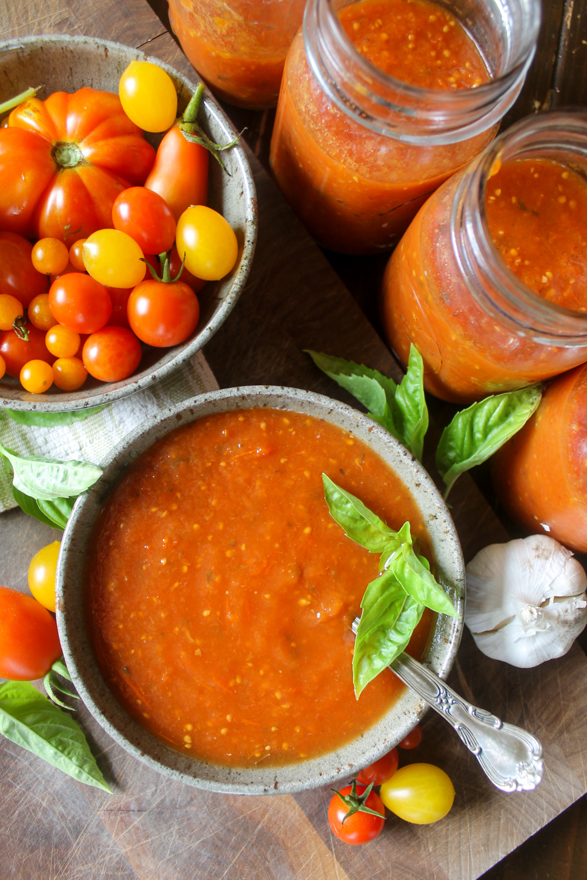 Slow cooker tomato sauce in a bowl with a bowl of tomatoes and jars of sauce.