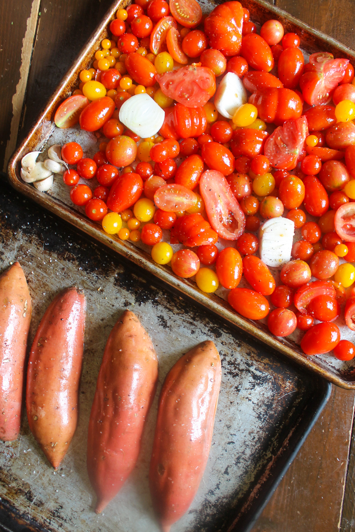 Tomatoes with onions and sweet potatoes on two sheet pans.