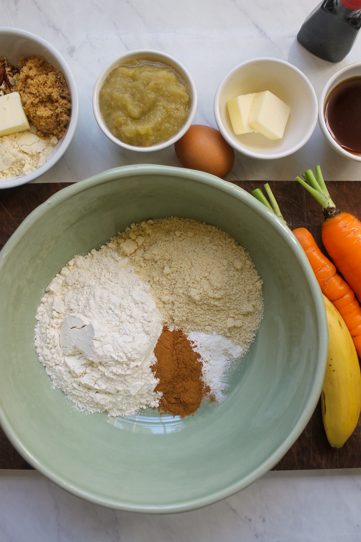 Dry ingredients for muffins in a bowl with other ingredients on a cutting board.
