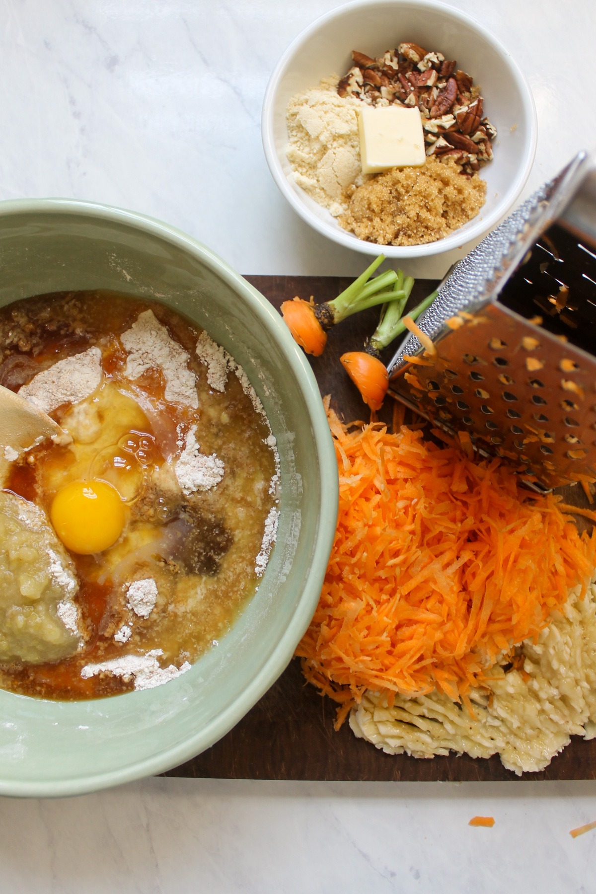 Ingredients in a bowl for muffin batter with shredded carrots and mashed banana on a cutting board.